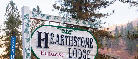 En skylt för Hearthstone Elegant Lodge, med en väg och träd i bakgrunden.