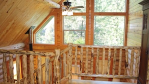 A wooden cabin with a loft bedroom, large windows, and a ceiling fan. - Hearthstone Elegant Lodge by the River (Kamiah)