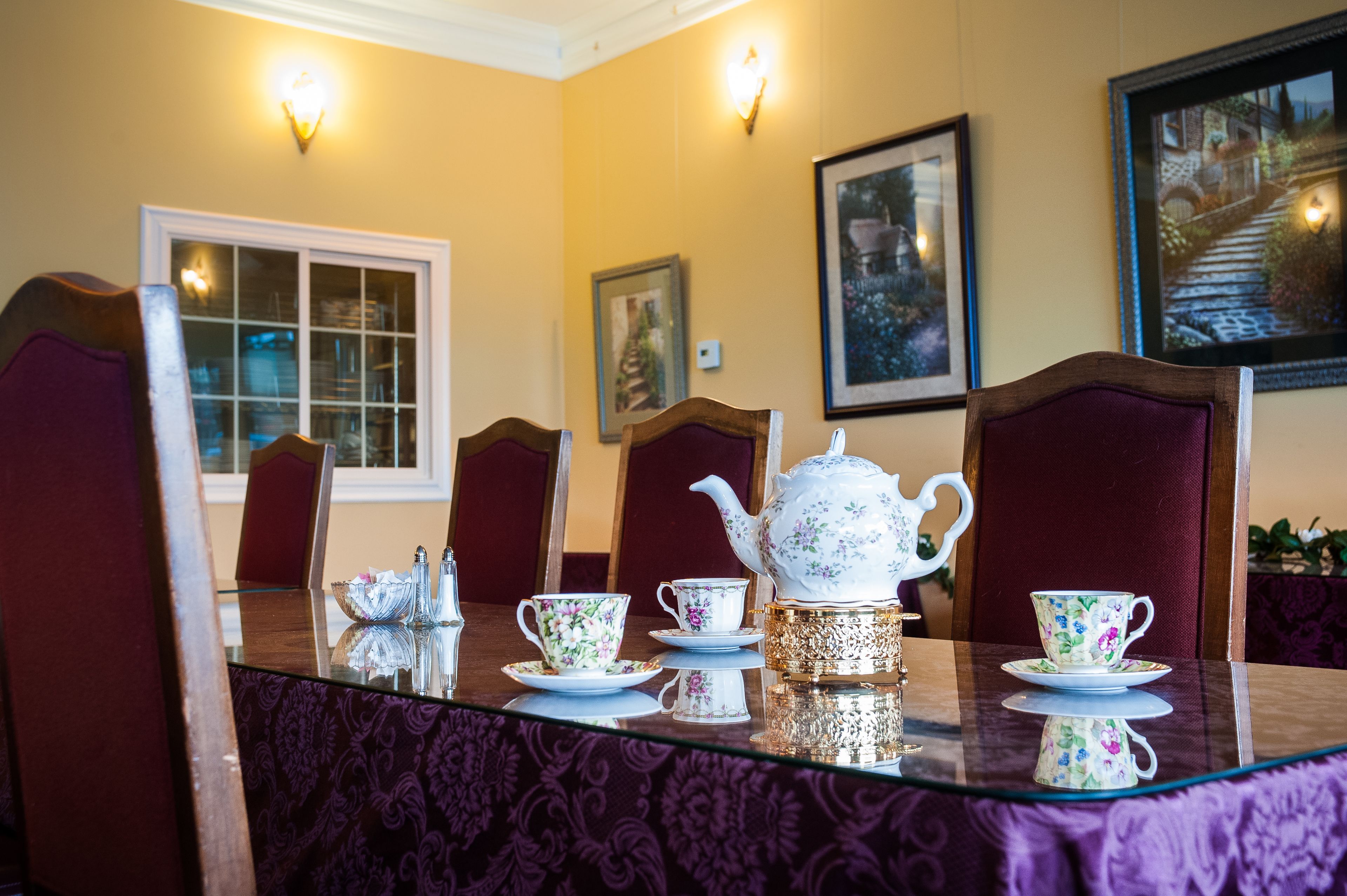 A dining table with floral tea set, red chairs, and wall-mounted lights.