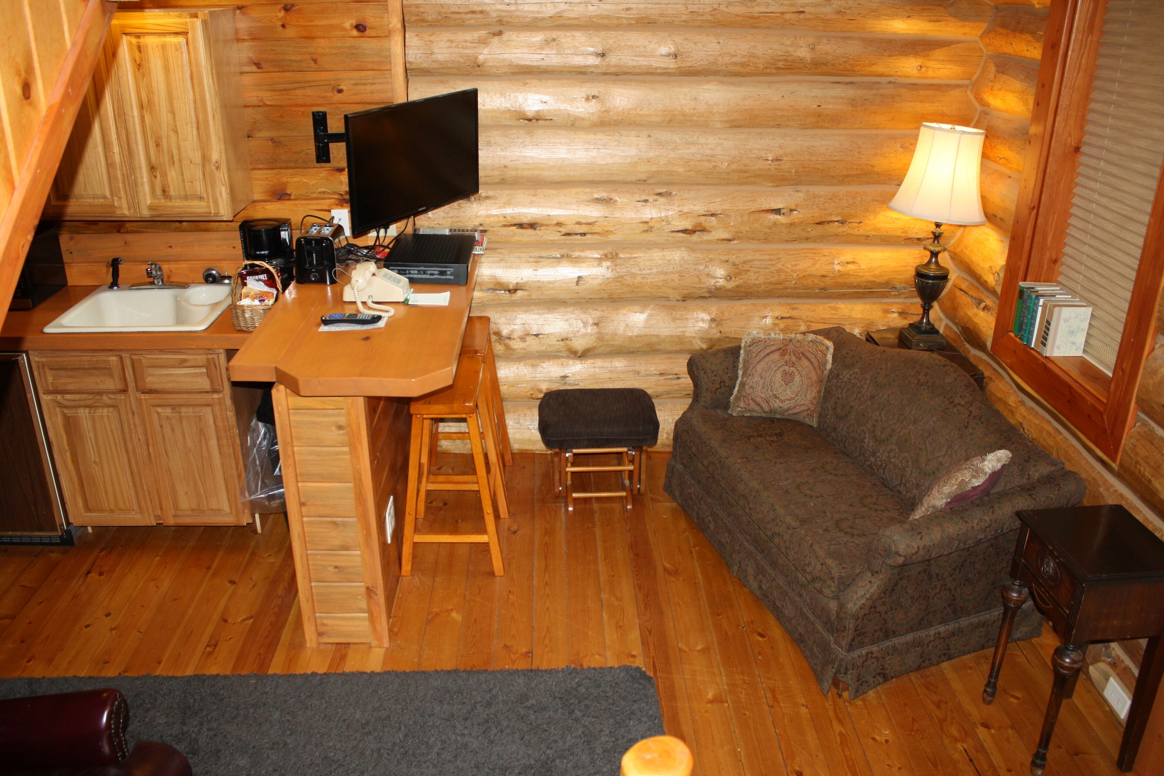 A cozy log cabin interior with a kitchen area, a dining table, a sofa, and a lamp.