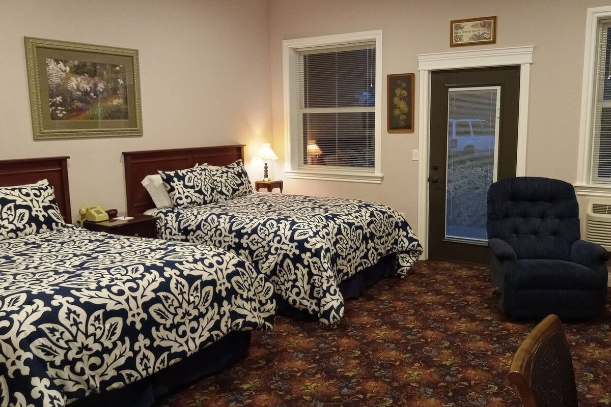 A hotel room with two beds, a chair, a door, and a window with blinds.