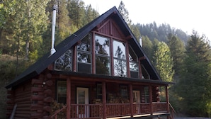 A log cabin with a large front porch, multiple windows, and a chimney. - Hearthstone Elegant Lodge by the River (Kamiah)