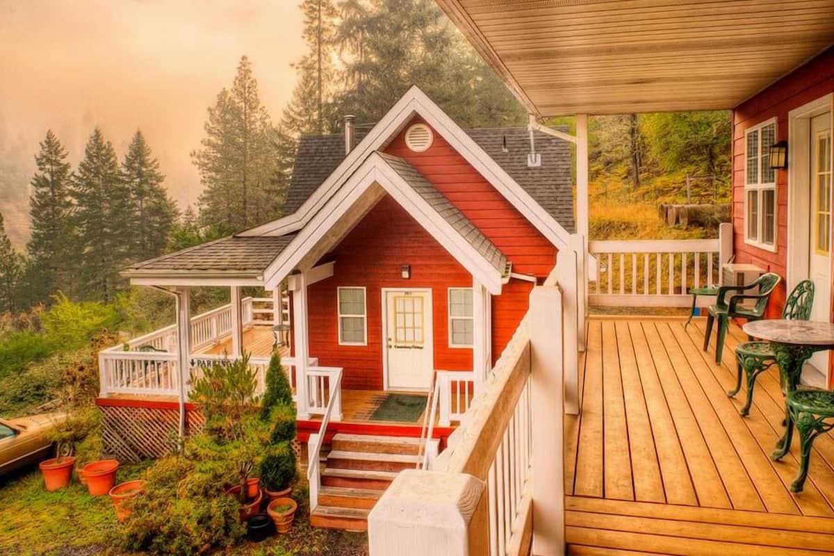 A red cabin with a wooden deck, a porch, and a small garden area.