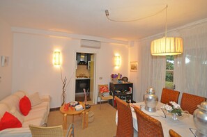 A living room with a sofa, dining table, chairs, and a chandelier. - Mariasole (Castiglione della Pescaia)