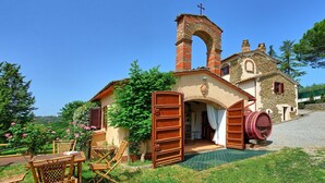 A rustic building with a brick chimney, a wooden barrel, and a large open door. - Uccellaia (Magione)