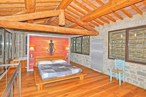 A bedroom with a wooden bed, a stone wall, and a large window.