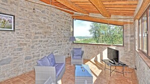 A stone-walled room with wooden beams, a large window, wicker furniture, and a laptop on a stand. - Villa Ferdinando (Poggibonsi)