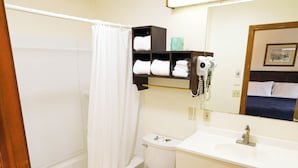 Un baño con bañera, inodoro y lavabo. Cuenta con una cortina de ducha, un perchero y un secador de pelo.