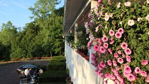 Un edificio con un balcón cubierto de flores rosadas, un camino de entrada pavimentado y un coche estacionado al fondo.