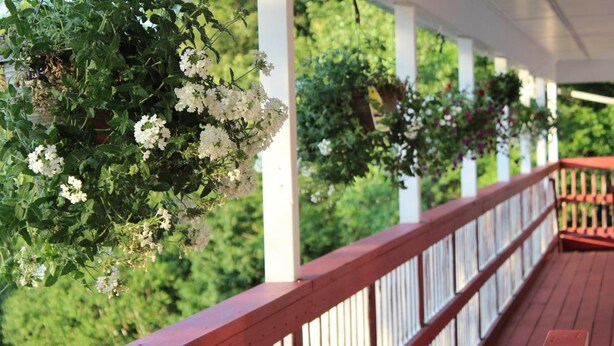 Una terraza de madera con barandas blancas y cestas de flores colgantes.