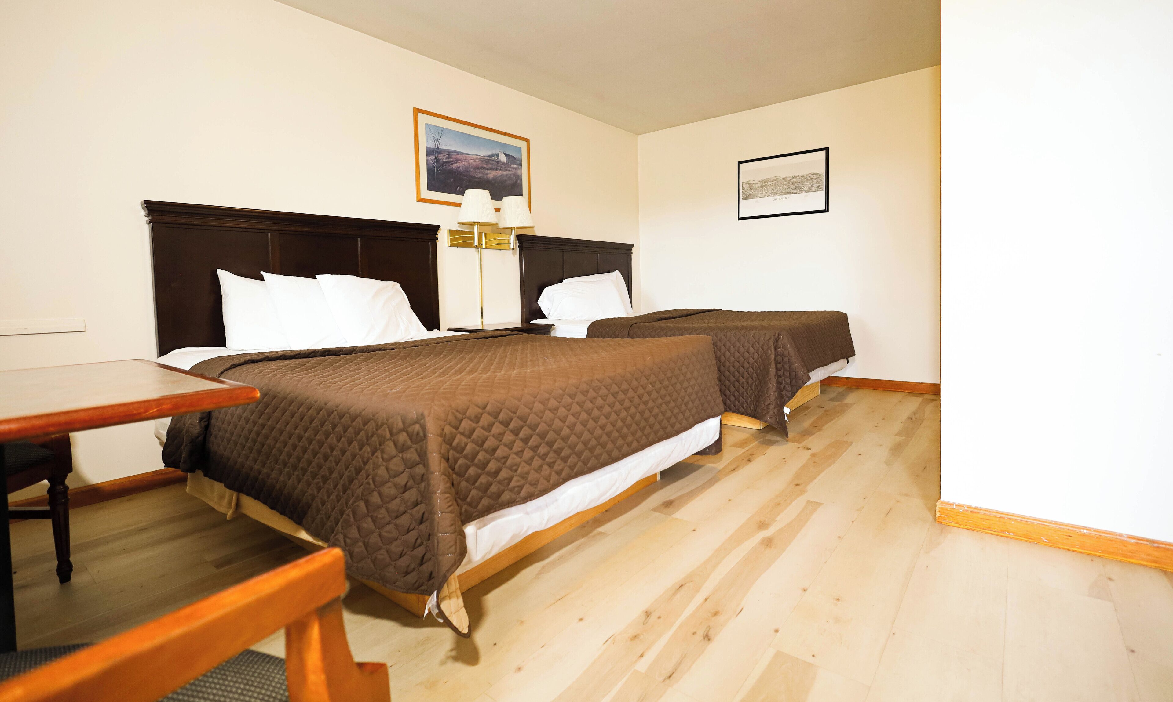Ein Hotelzimmer mit zwei Betten, einem Holztisch und einem gerahmten Bild an der Wand.