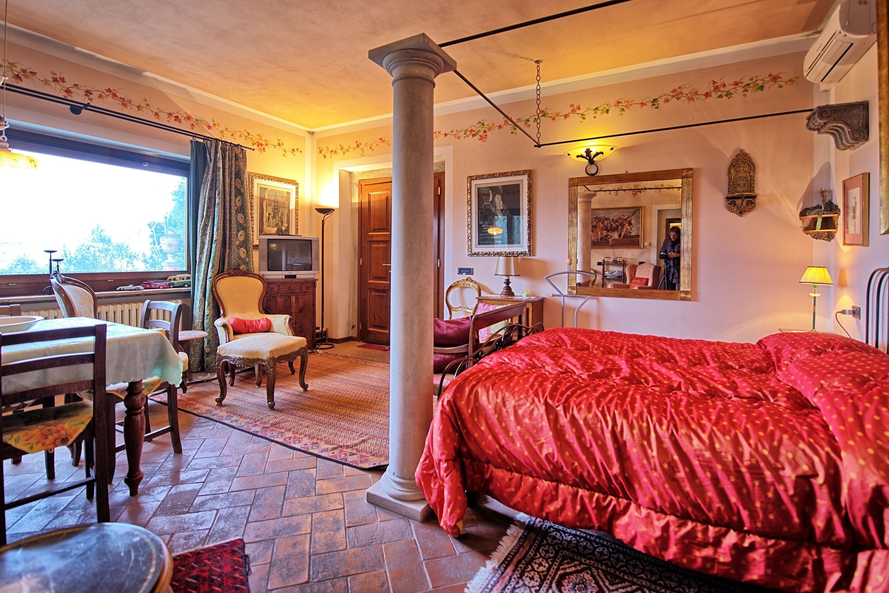 A room with a large bed, a dining table with chairs, a television, and a window with curtains.