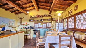 A rustic kitchen with wooden beams, a dining table set for four, and a large window with a view. - Casa Vania (Reggello)