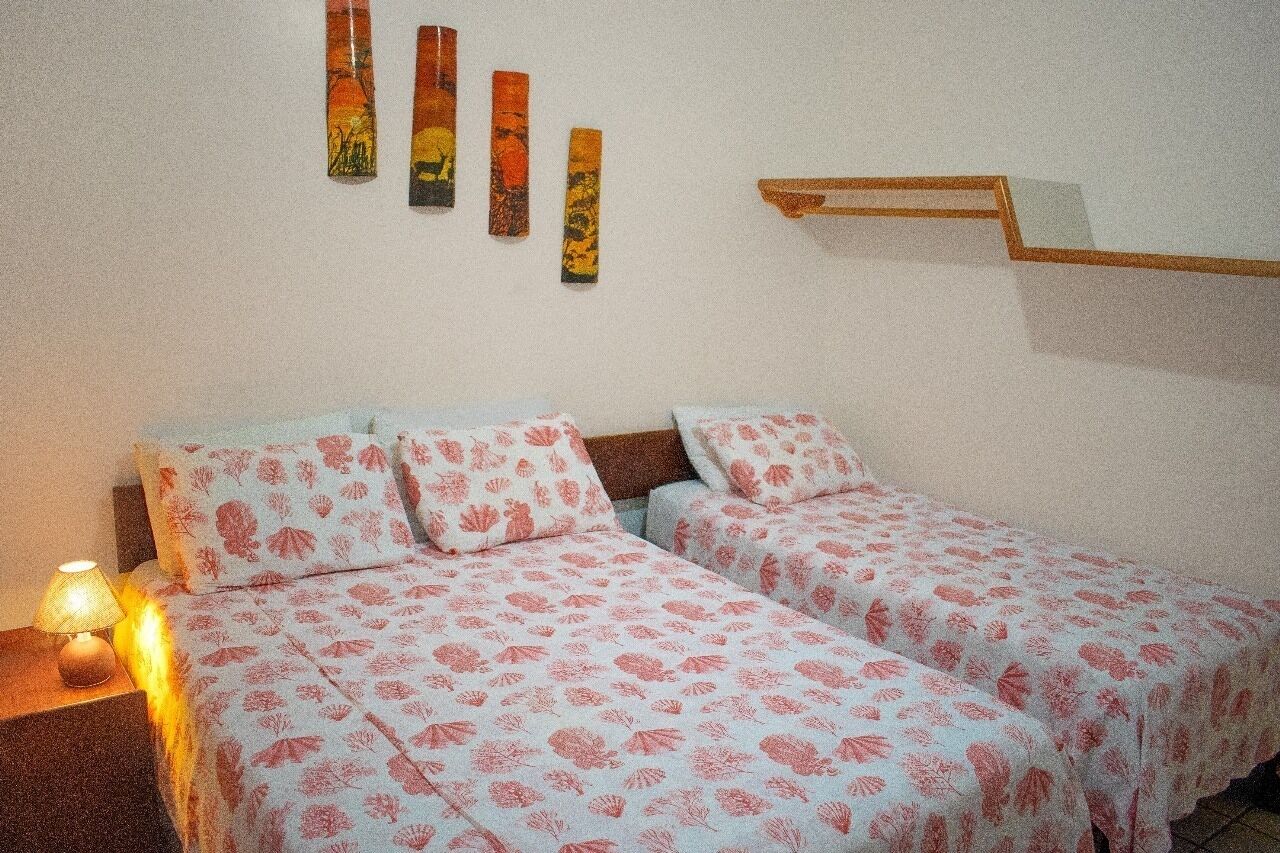 A double bed with floral bedding, a bedside table with a lamp, and a wall-mounted shelf.