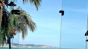 Une table recouverte d’une nappe à carreaux, une chaise en métal et une vue sur la mer et la terre au loin.