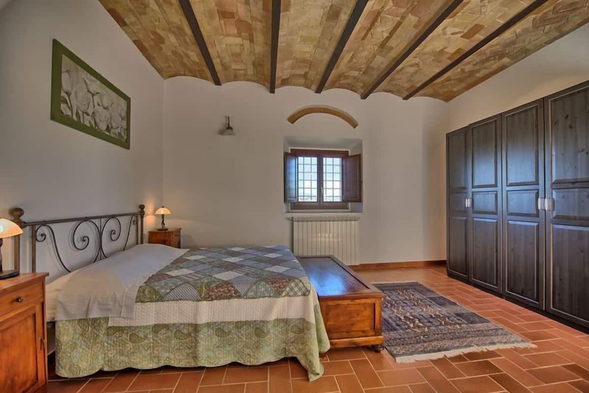 A bedroom with a bed, a nightstand, a dresser, a window, and a radiator.