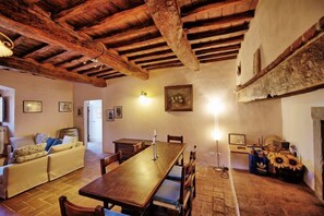 A rustic room with exposed wooden beams, a wooden dining table, a sofa, and a fireplace.