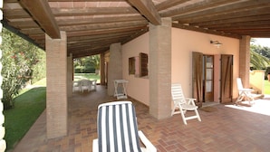 Un patio couvert avec un sol en briques, des fauteuils de jardin blancs et une table avec des chaises.