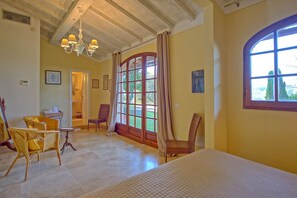 A spacious room with a large window, wicker furniture, a chandelier, and a bed.