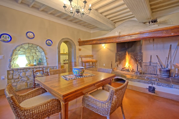 A dining area with a stone fireplace, wicker chairs, and a wooden table.