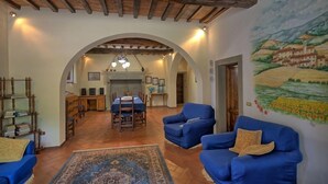 A spacious living area with a high ceiling, wooden beams, a dining table, blue sofas, and a mural of a landscape. - Palazzo Rosadi (Monterchi)