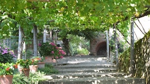 A stone staircase leading up to a covered area with a brick archway, surrounded by potted plants and greenery. - Palazzo Rosadi (Monterchi)