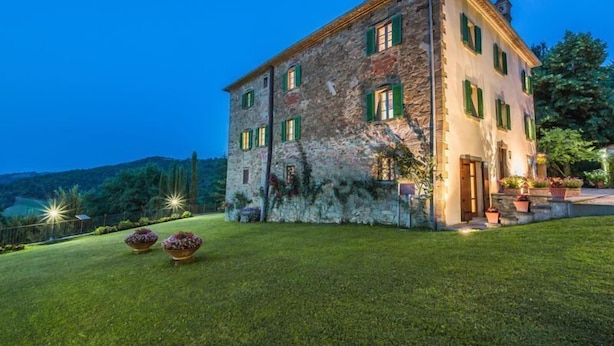 A stone building with green shutters, a well-maintained lawn, and outdoor lighting. - Palazzo Rosadi (Monterchi)