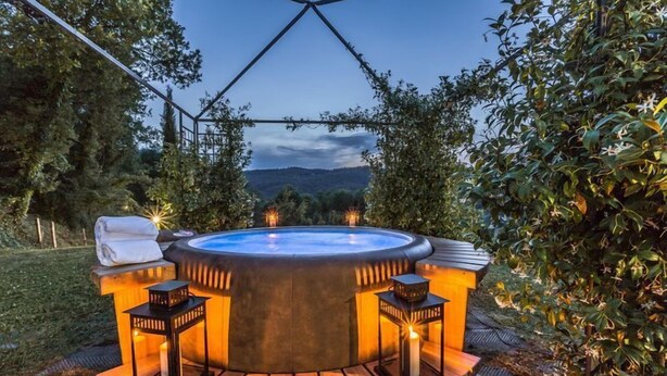 Een hottub met een houten terras en lantaarns, omringd door groen en uitzicht op heuvels.