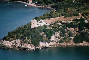An aerial view of a coastal property with a prominent tower, lush greenery, and a rocky shoreline.