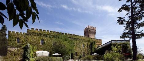 A castle-like building with ivy-covered walls, a central tower, and a paved courtyard with a pathway leading to the entrance.