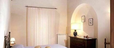Un dormitorio con cama, mesita de noche, cómoda y un arco de entrada.