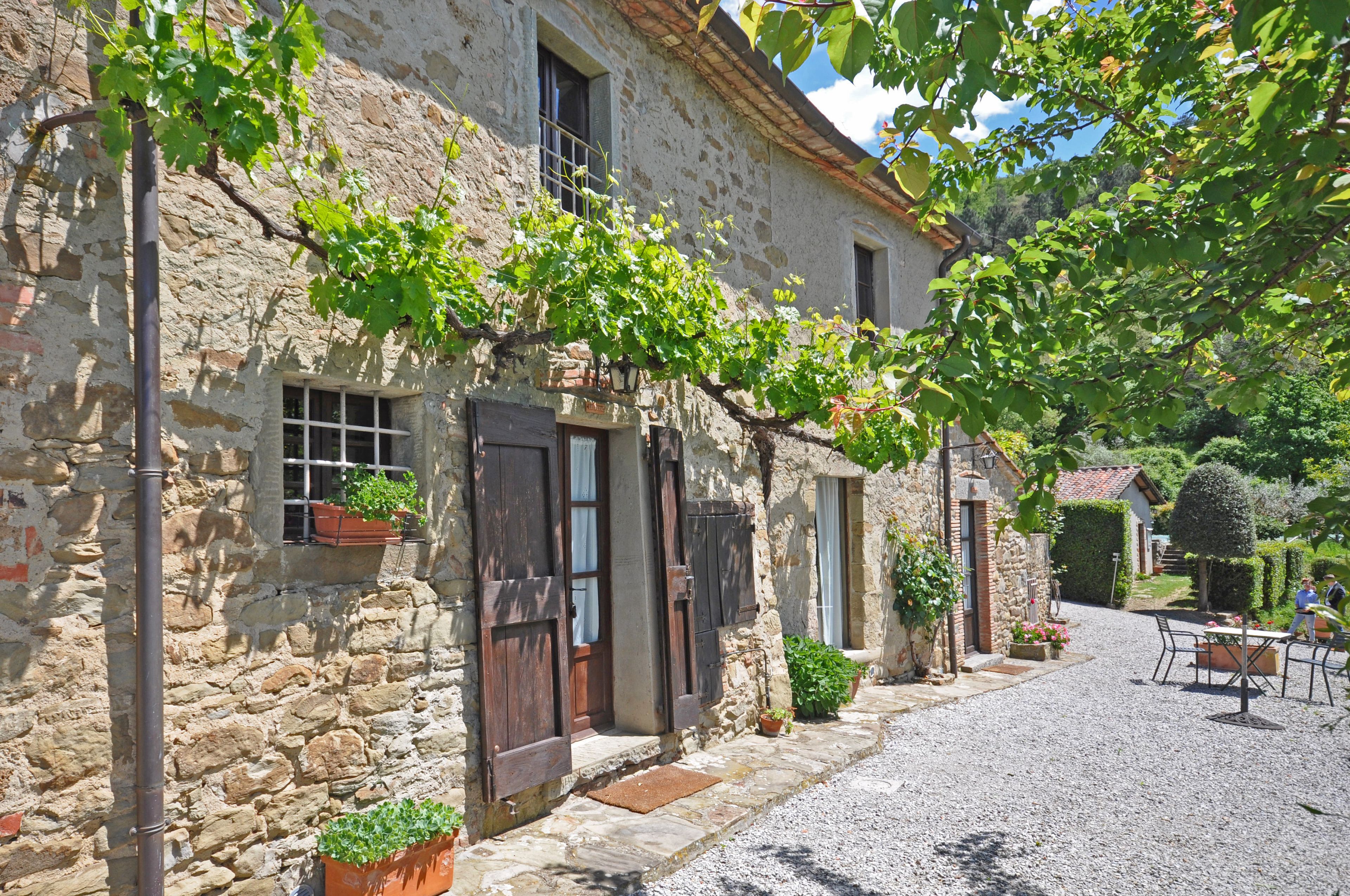 Un edificio de piedra con encanto rústico, con camino de grava y plantas en macetas.