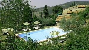 A swimming pool surrounded by greenery, with lounge chairs and striped umbrellas. - Borgo Del Castagno (Cortona)