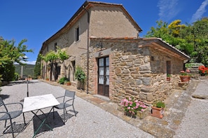 A stone building with a small patio area, a table, and chairs. - Borgo Del Castagno (Cortona)