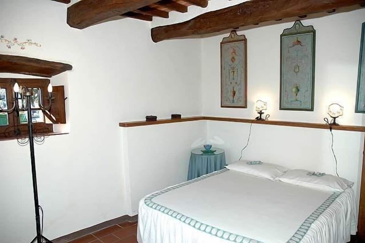 Un dormitorio con una cama, una mesita redonda y un estante en la pared.