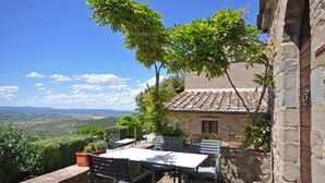 A stone building with a tiled roof, outdoor seating, and a view of the countryside. - Borgo Del Castagno (Cortona)