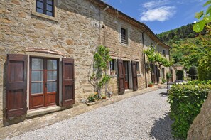 A stone building with wooden shutters, a gravel path, and potted plants. - Borgo Del Castagno (Cortona)