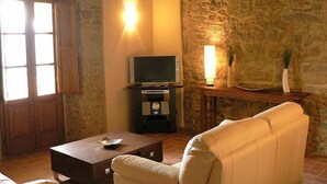 Una sala de estar acogedora con una pared de piedra, un televisor sobre un mueble bajo, un sofá y una mesita con un cuenco.