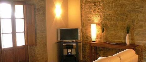 A cozy living room with a stone wall, a television on a stand, a sofa, and a small table with a bowl.