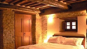 Un dormitorio con pared de piedra, vigas de madera en el techo, una puerta de madera y una ventana con vistas.
