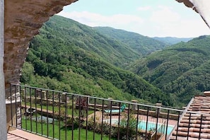 A balcony with a view of lush green hills and a pool area.
