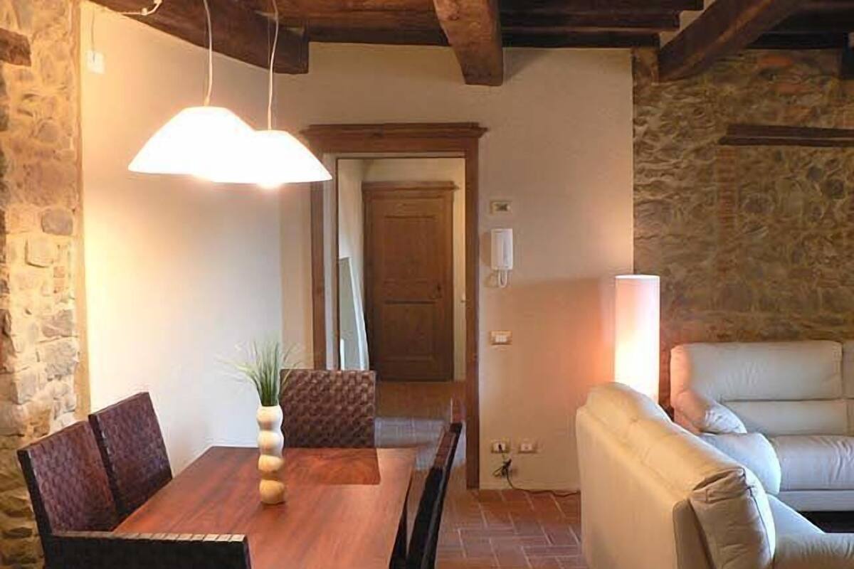 Un comedor con una mesa y sillas de madera, una planta en maceta y una lámpara colgante.