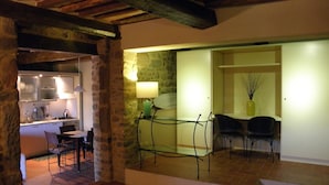 Una cocina moderna con paredes de piedra, una zona de comedor con separador de vidrio y una escalera que sube a otro nivel.