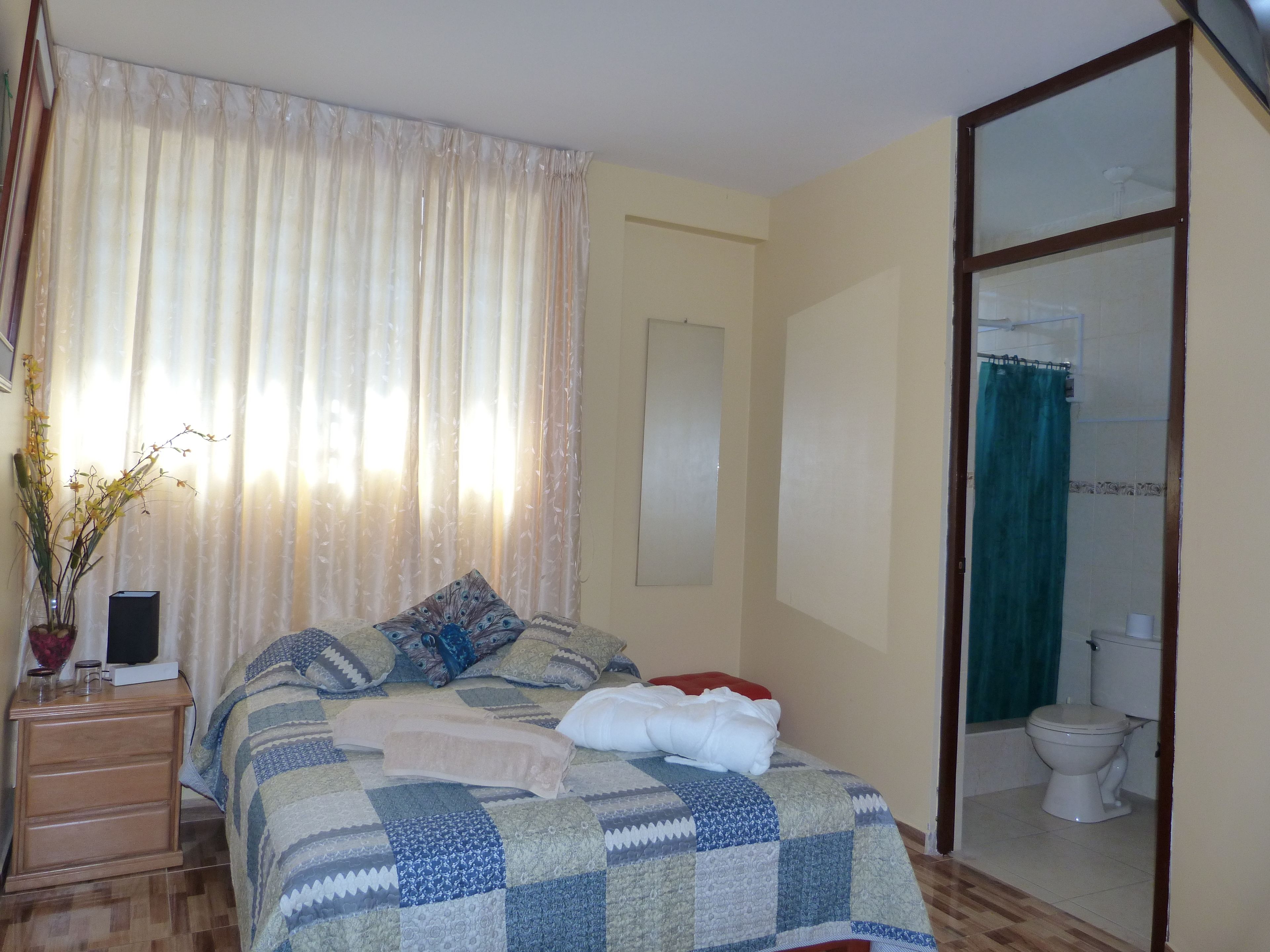 Une chambre à coucher avec un lit, une table de chevet avec une lampe, une fenêtre avec des rideaux et une vue sur la salle de bain.