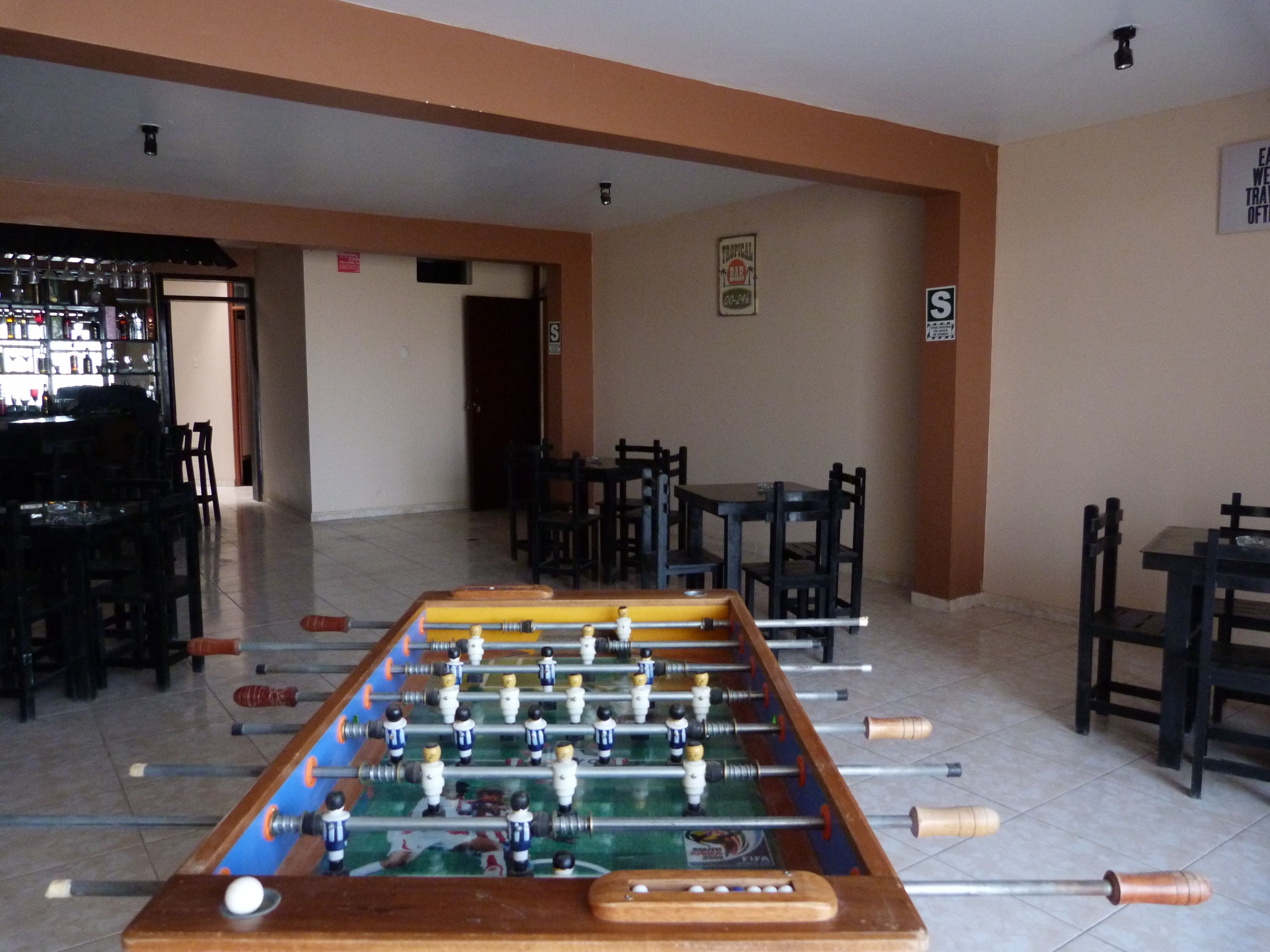 A foosball table in a room with a bar area and several tables and chairs.