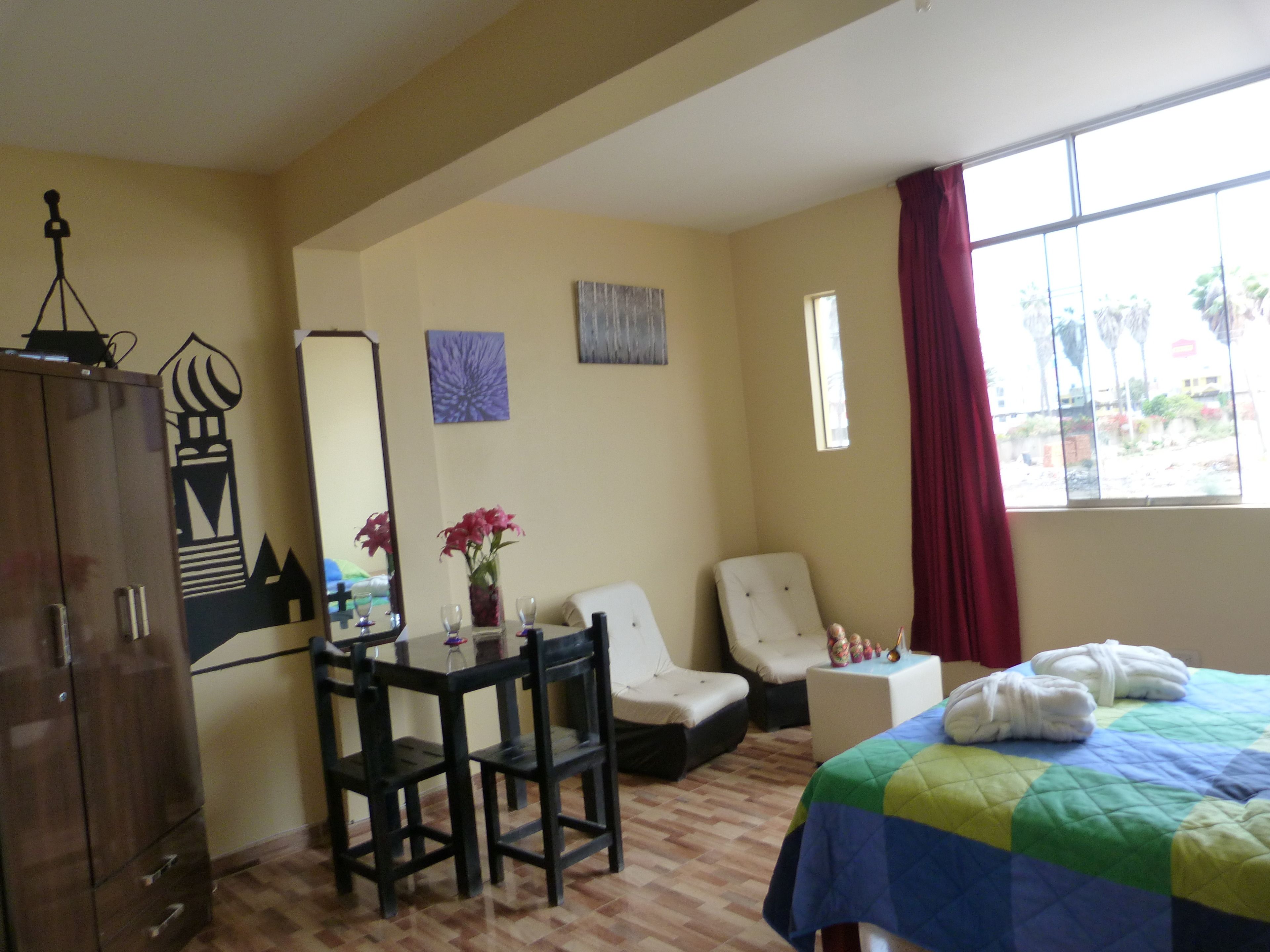 A hotel room with a bed, a desk with chairs, a wardrobe, a window with a view, and artwork on the walls.