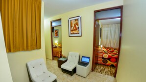 A hotel room with a bed, two white armchairs, a small table with a laptop, and a colorful sofa. - Matryoshka (Ica)