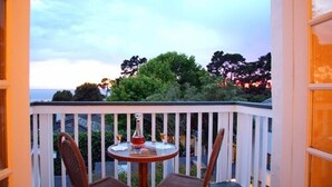 A balcony with a round table and two chairs, overlooking a scenic view of trees and the ocean. - Monte Verde Inn (Carmel)