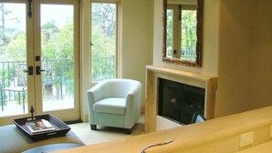 A room with a white armchair, a fireplace, and a large mirror on the wall. - Monte Verde Inn (Carmel)