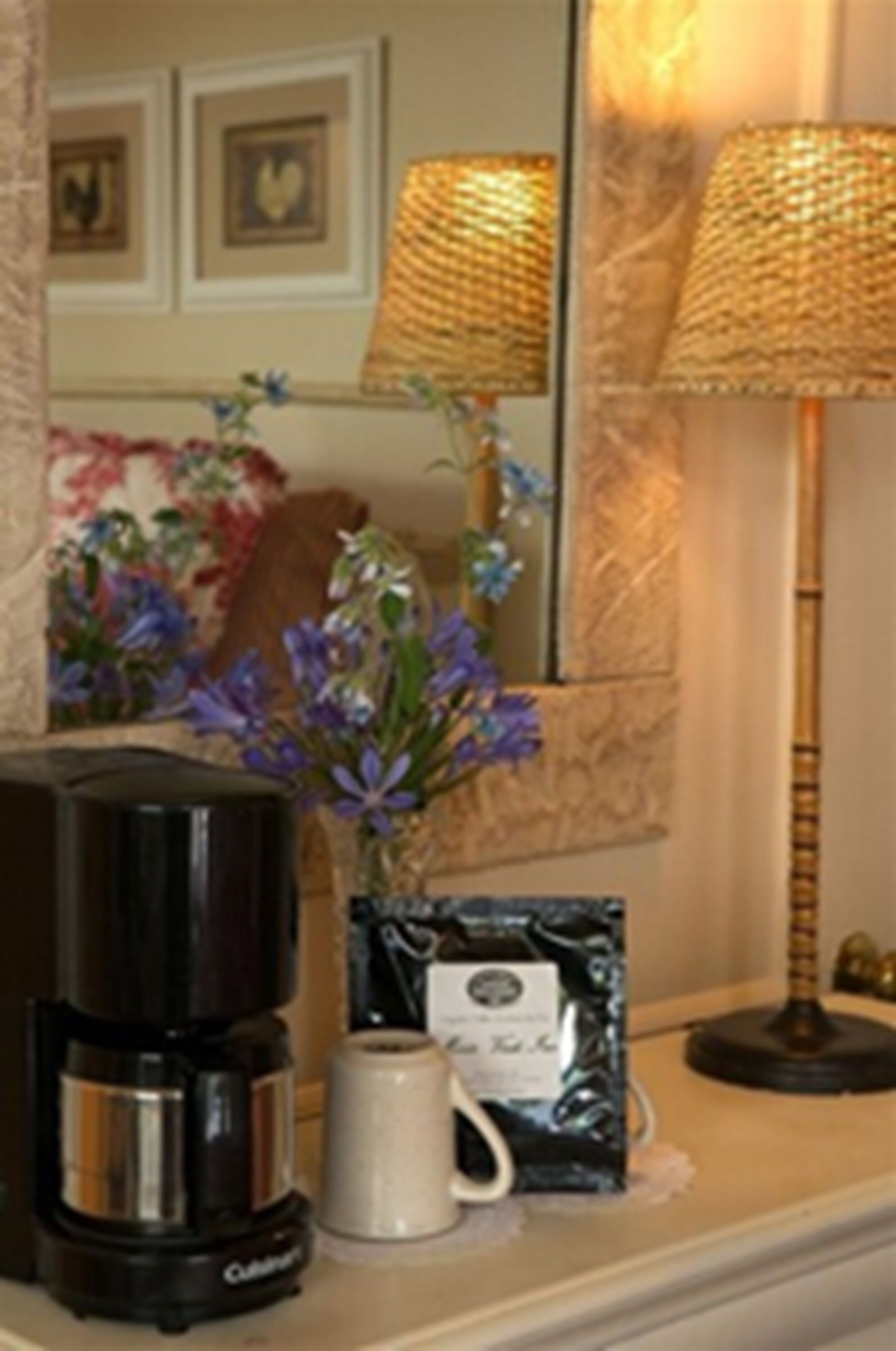 A coffee maker, a mug, a decorative vase with flowers, and a lamp on a table.
